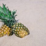 Two fresh pineapples resting on a sunny sandy beach, evoking tropical vibes.